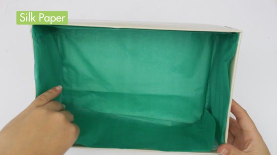 a person is holding up a green paper box with the bottom half open and one hand reaching for it