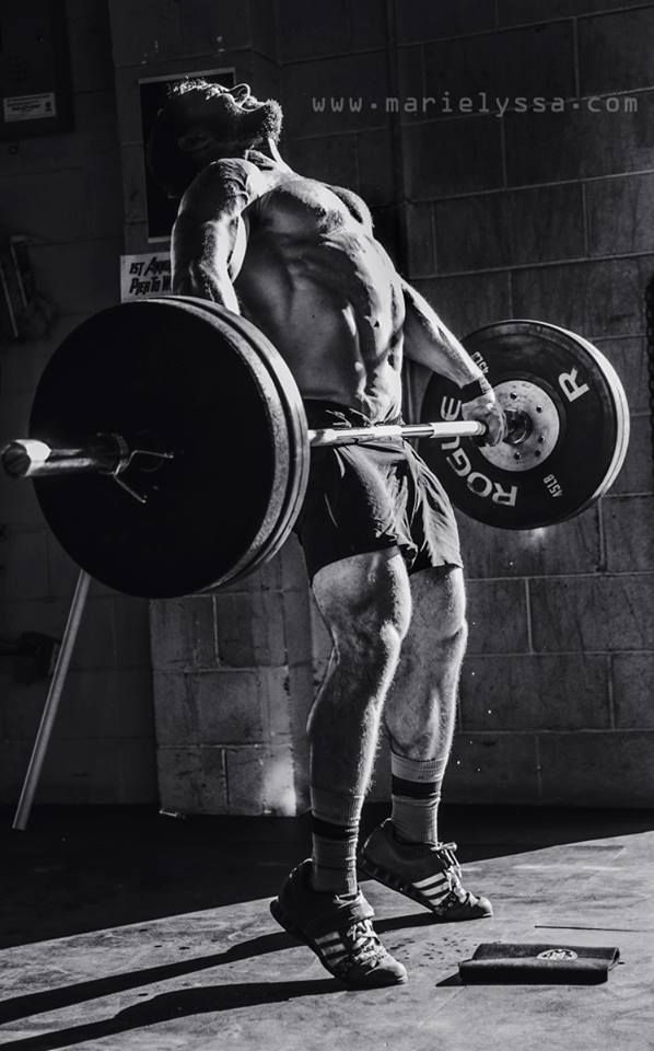 a man holding a barbell while standing next to a brick wall