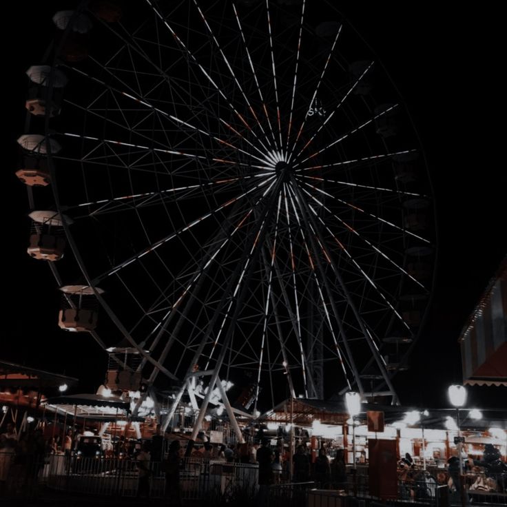 a large ferris wheel sitting next to a tall building on top of a dark sky