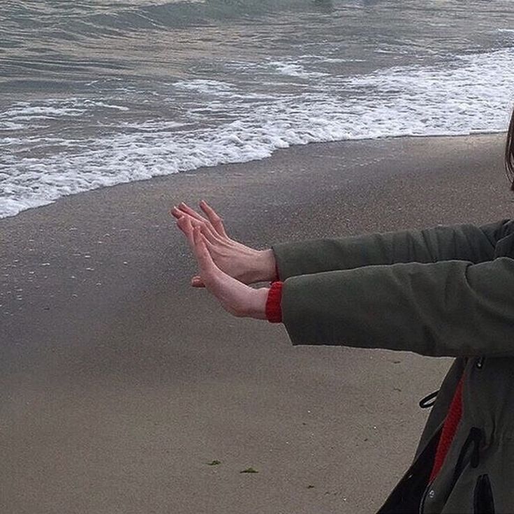 a woman standing on top of a beach next to the ocean holding her hands out