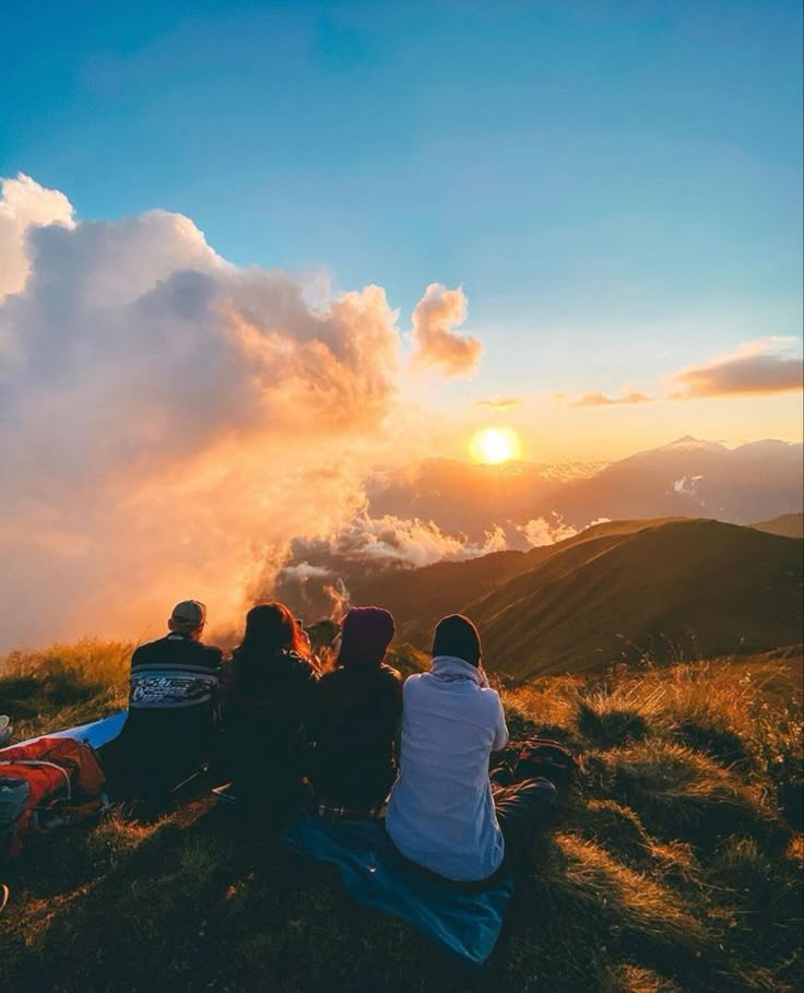 three people sitting on top of a hill watching the sun go down in the distance