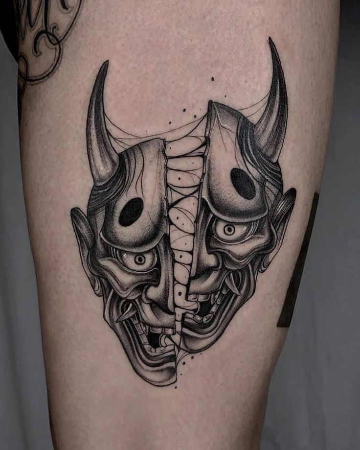 a black and white image of two horned masks on the thigh, one with horns