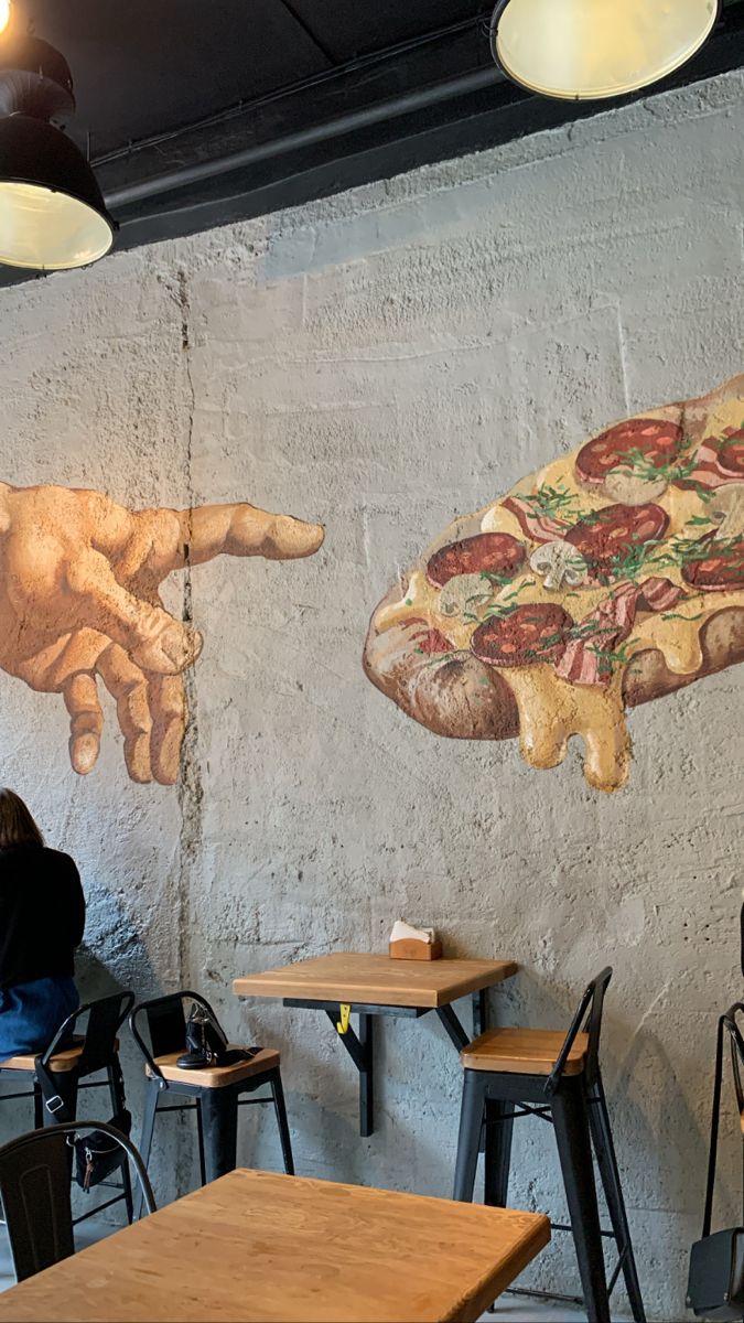 two people sitting at tables in front of a wall mural with pizza and hands on it