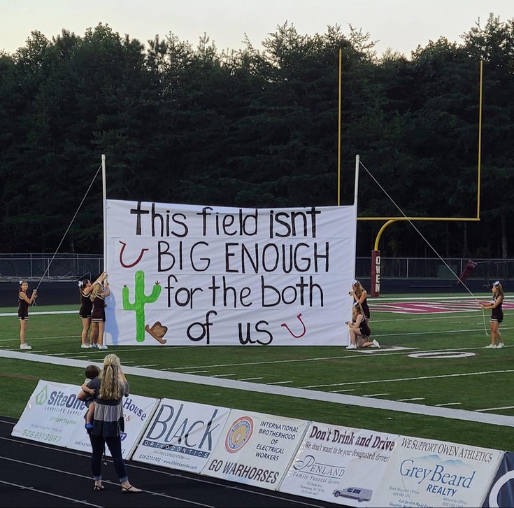 a group of people standing on top of a field holding up a sign that reads, this field isn't big enough for the both of us