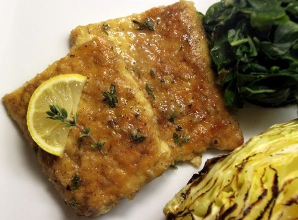 some food on a white plate with greens and lemons next to eachother