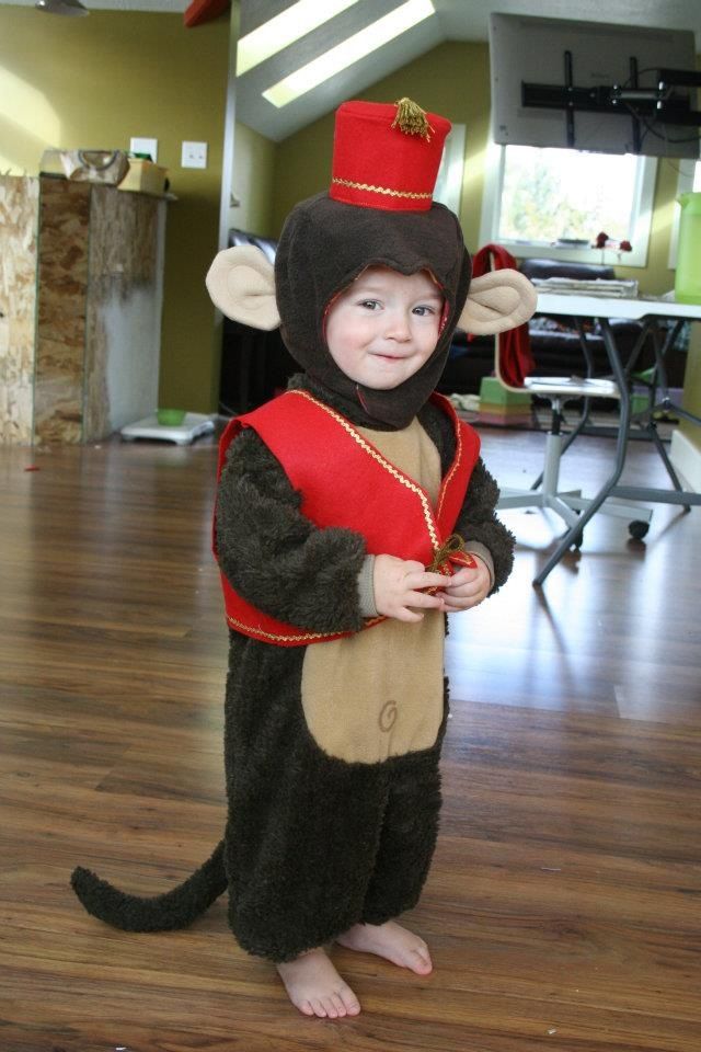 a child in a monkey costume standing on a hard wood floor wearing a red top hat