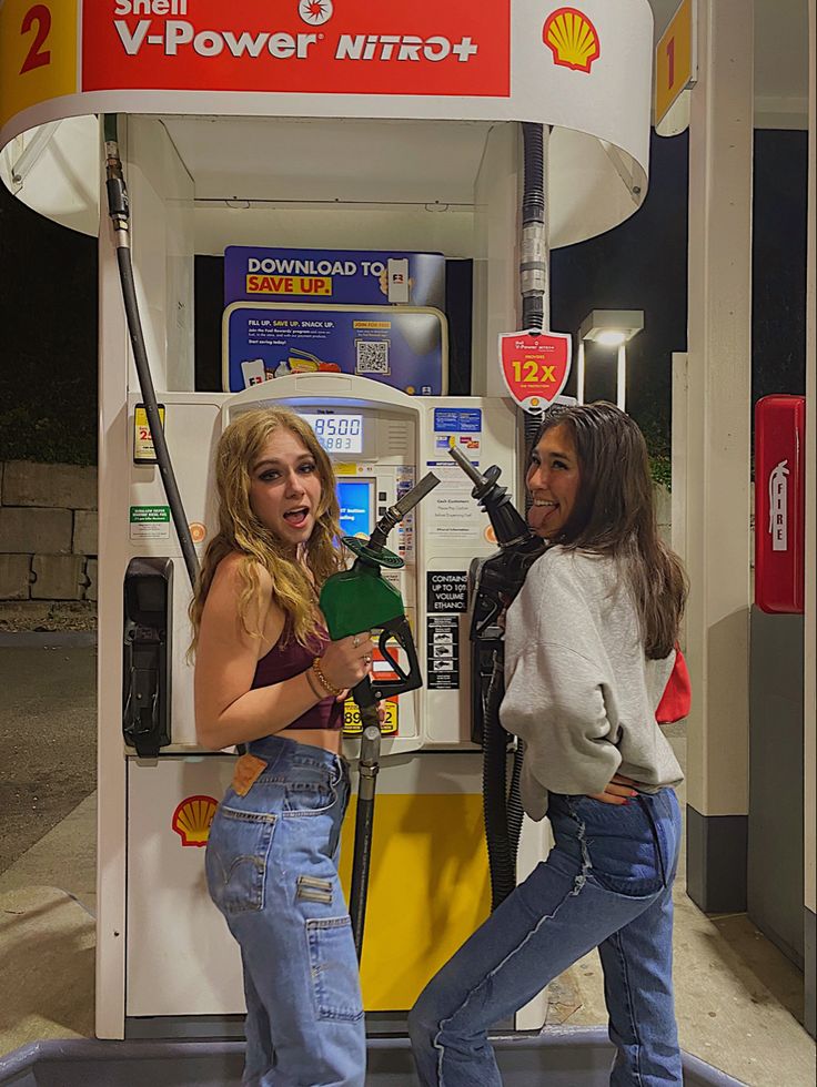 two girls standing in front of a gas pump