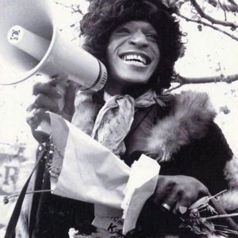 a man holding a megaphone in his right hand and laughing while standing next to a tree