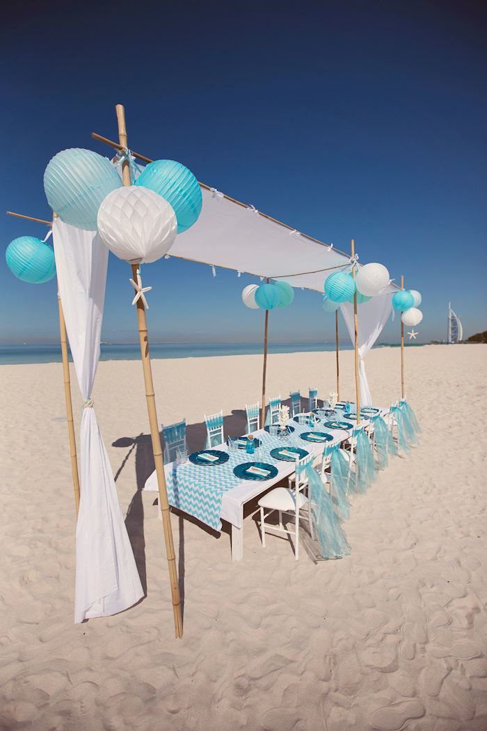 an outdoor table set up on the beach for a party with blue and white decorations