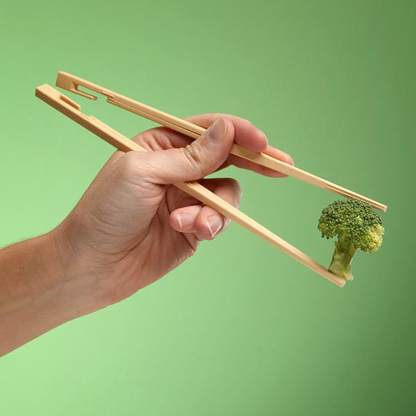 a hand holding chopsticks with a piece of broccoli sticking out of it