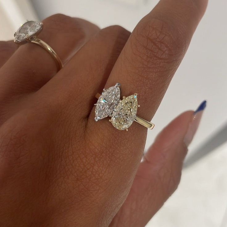 a woman's hand holding a ring with two pear shaped diamonds on top of it