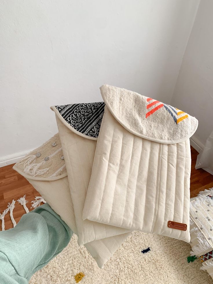 several pillows stacked on top of each other next to a white wall and wooden floor