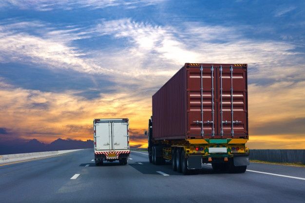 two trucks are driving down the highway at sunset