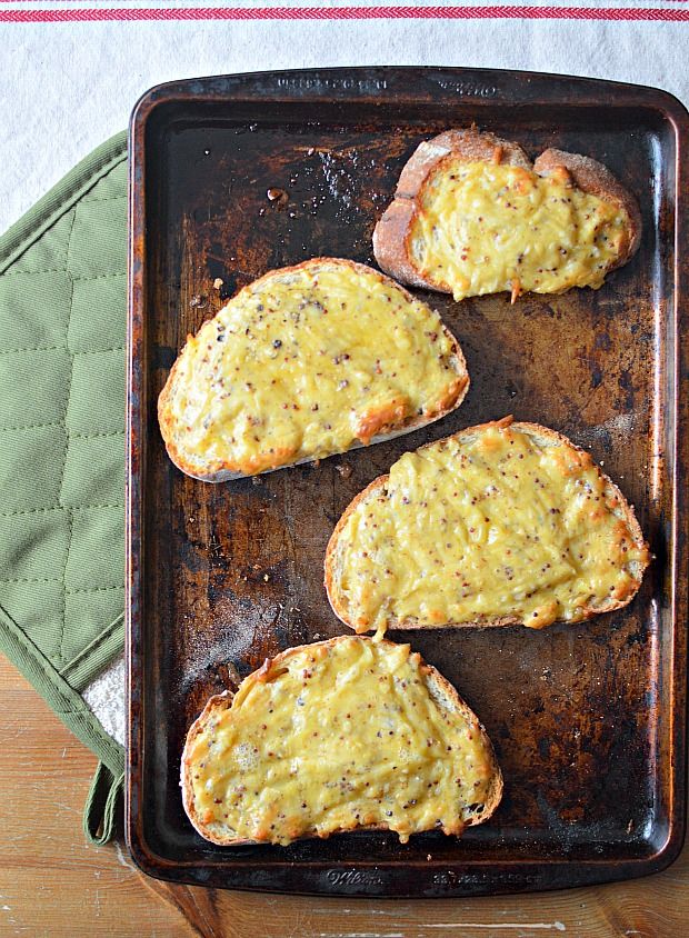 three pieces of bread with cheese on top sitting on a baking sheet next to an oven mitt