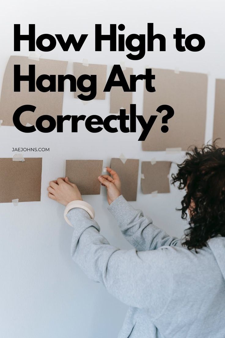 a woman painting on the wall with text overlay that reads how high to hang art correctly?