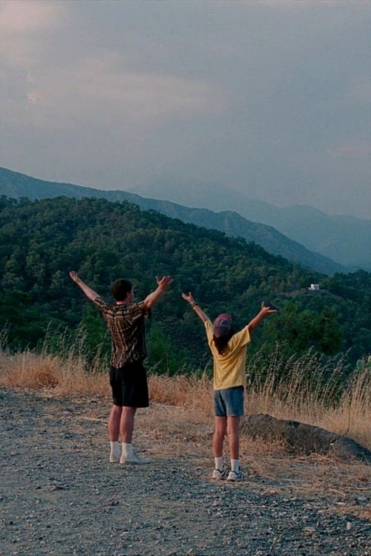 two people standing on top of a hill with their arms outstretched