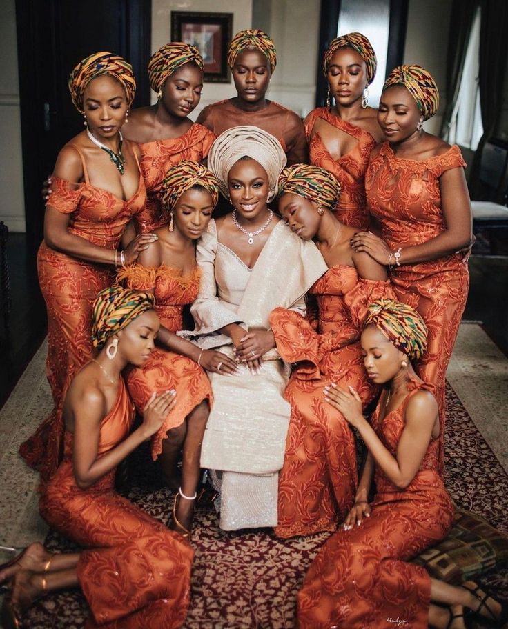 a group of women in orange dresses posing for a photo with one woman sitting on the floor