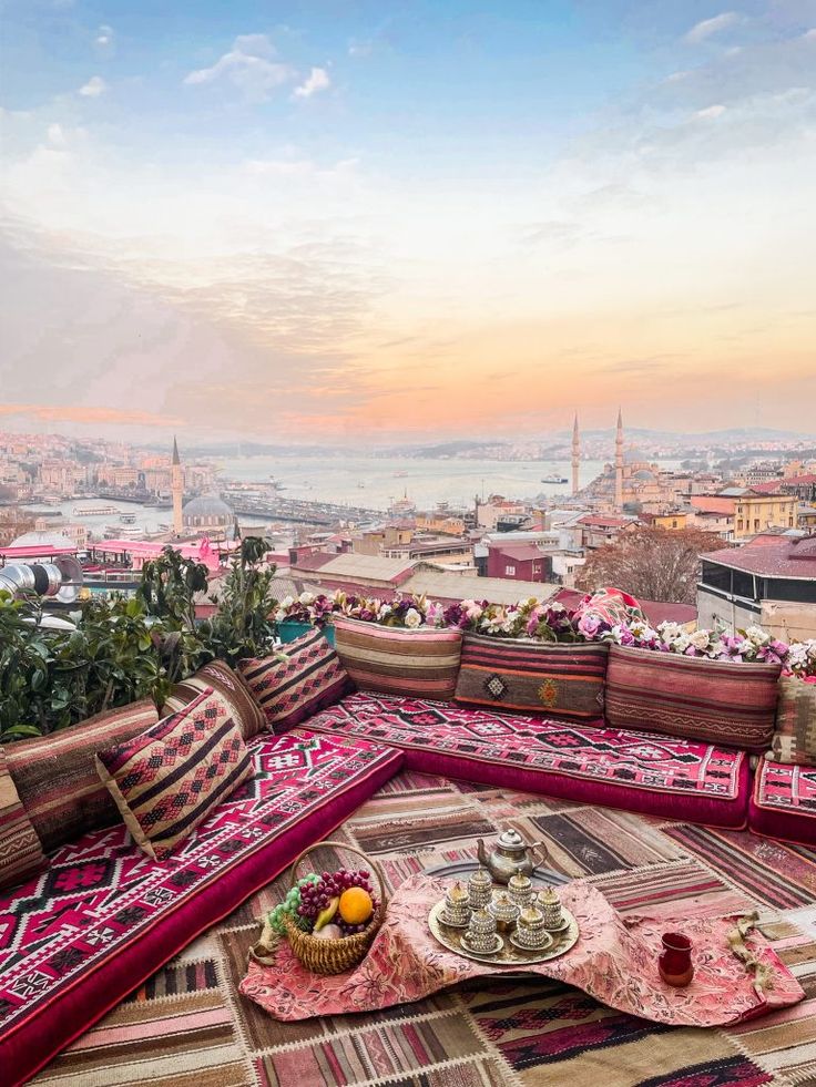 an outdoor seating area on top of a building with pink and green rugs in the foreground