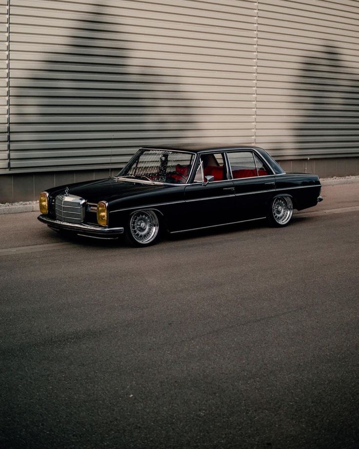 an old black car parked in front of a building next to a wall with shadows on it