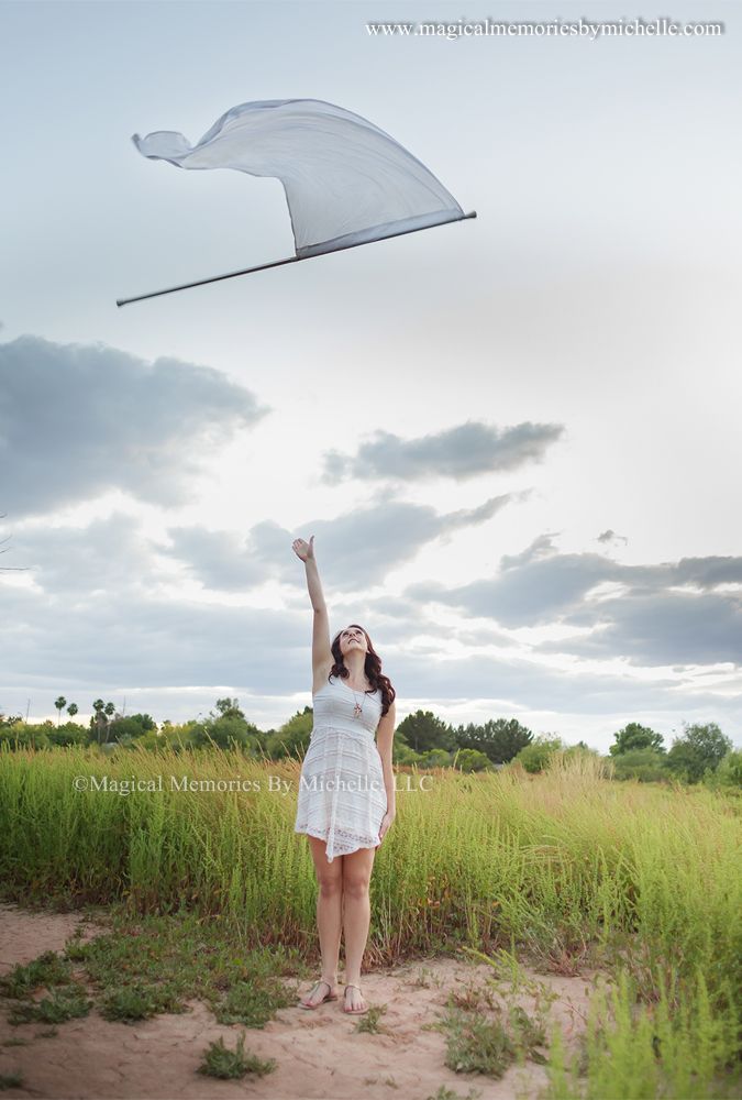 a woman in white dress flying a kite on top of a grass covered field at sunset