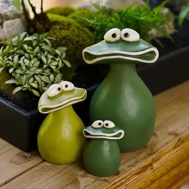 three ceramic birds sitting next to each other on top of a wooden table with plants in the background