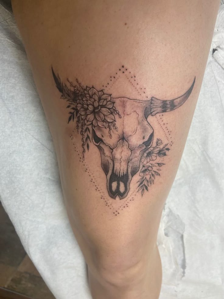 a tattoo on the leg of a woman with flowers and a bull's head