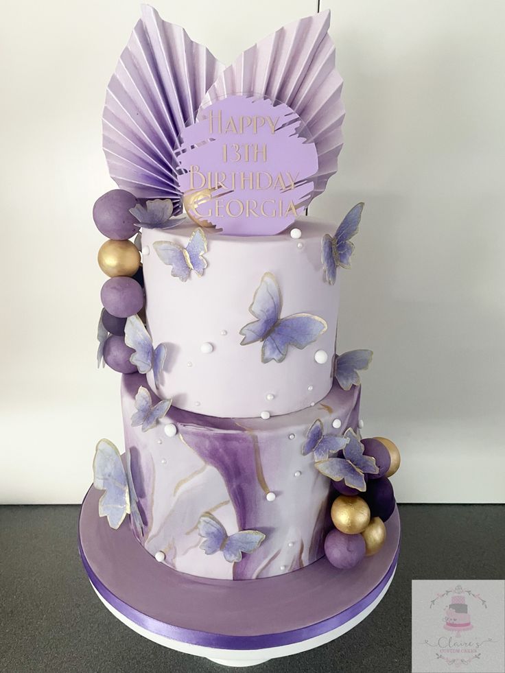 a three tiered cake decorated with purple and gold butterflies on the top, sitting on a table