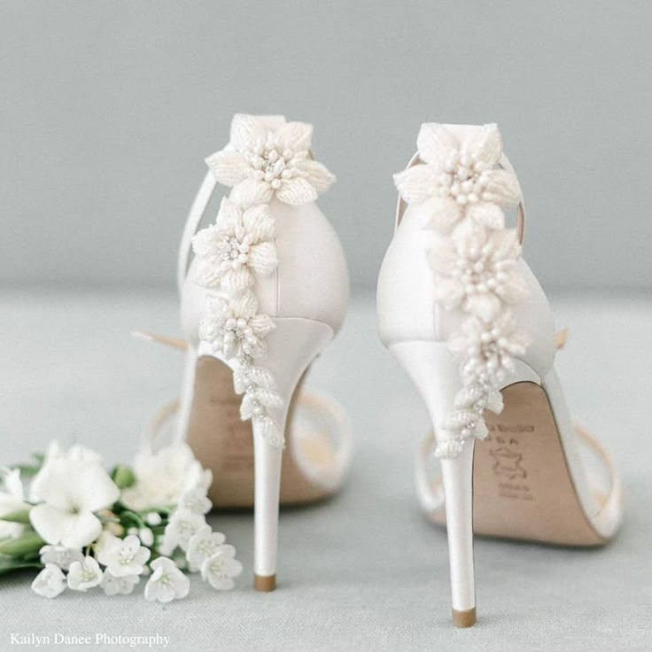 the bride's shoes are adorned with white flowers and pearls, while the bridal bouquet sits next to them