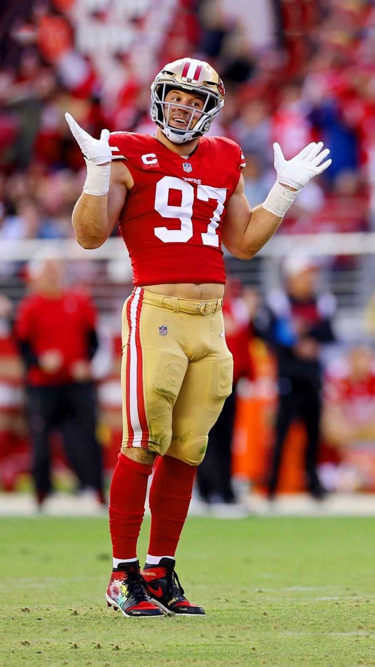 a football player is standing on the field with his hands in the air and looking at the camera