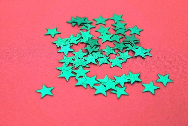 small green stars are scattered on a red surface, as if they were cut from paper