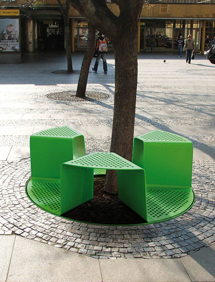 a green bench sitting under a tree on a sidewalk