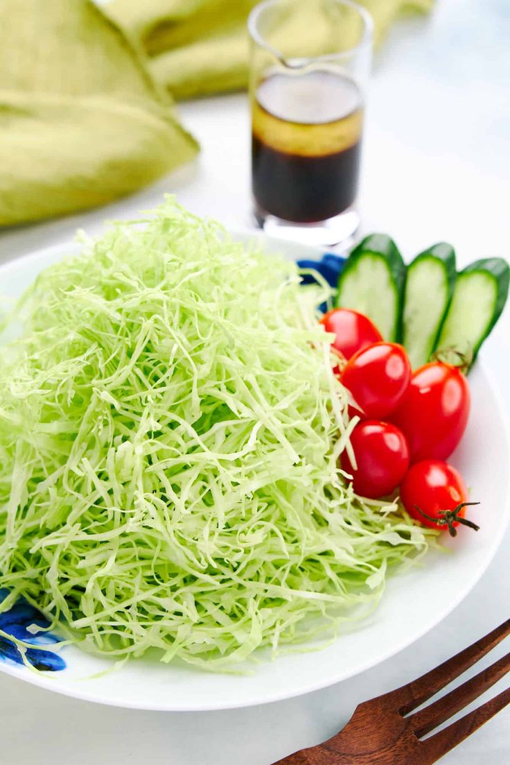 a white plate topped with lettuce and tomatoes next to a glass of soda