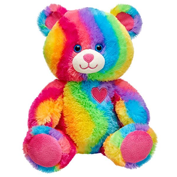 a rainbow colored teddy bear with heart on it's chest, sitting up against a white background