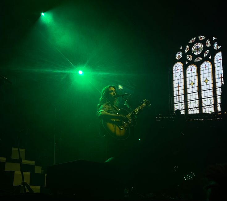 a man with a guitar on stage in front of a stained glass window at night