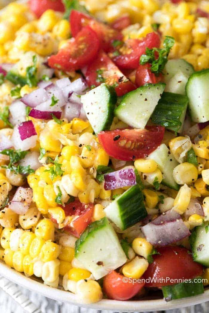 corn salad with cucumbers, tomatoes, and onions in a white bowl