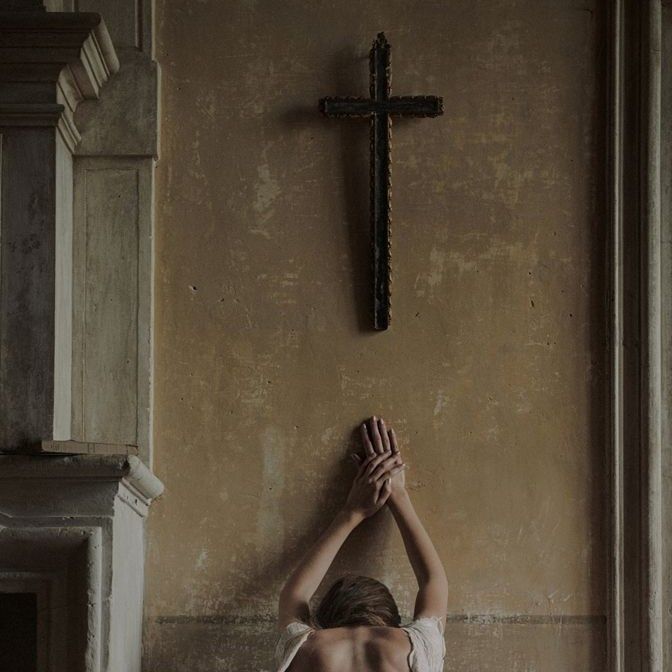 a woman kneeling down in front of a cross