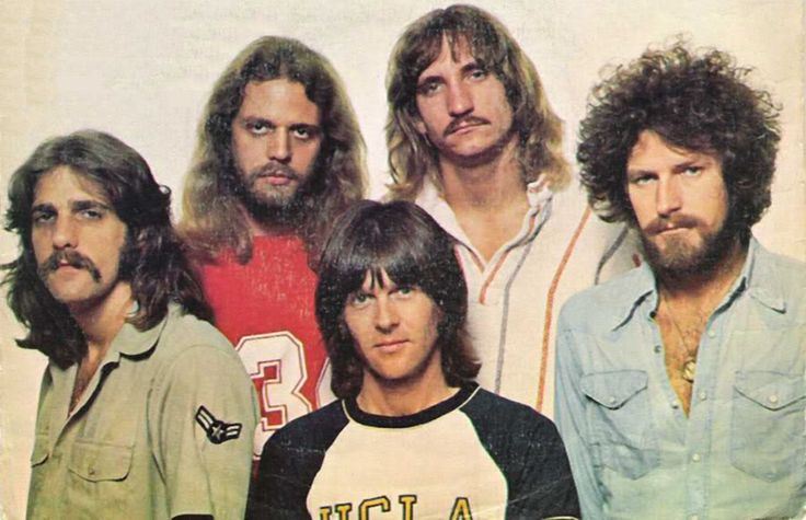 an old photo of four men with long hair and beards standing in front of a white background