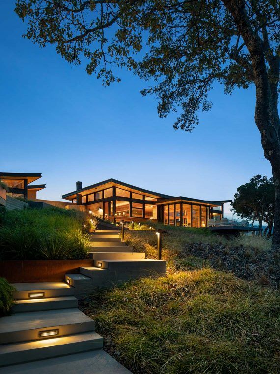 the stairs lead up to this modern house at night with lights shining on them and grass in front