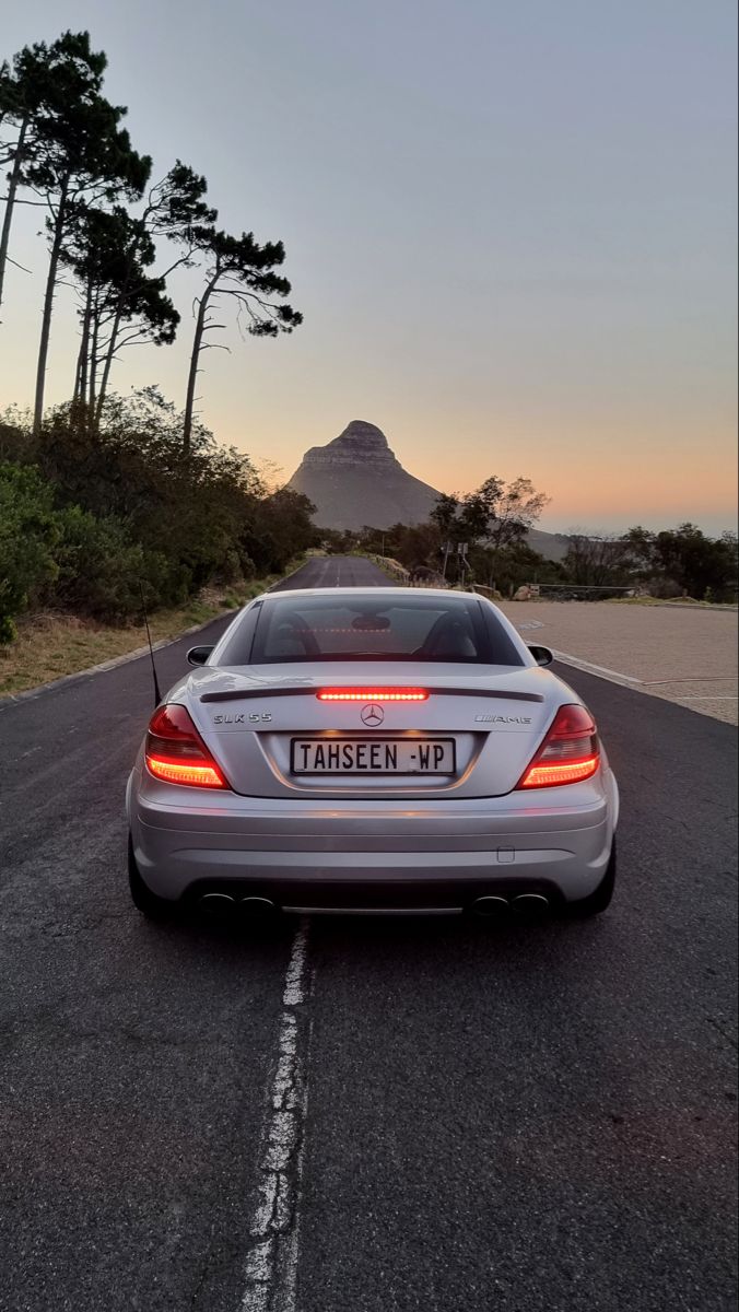 a silver car is parked on the side of the road near some trees and mountains