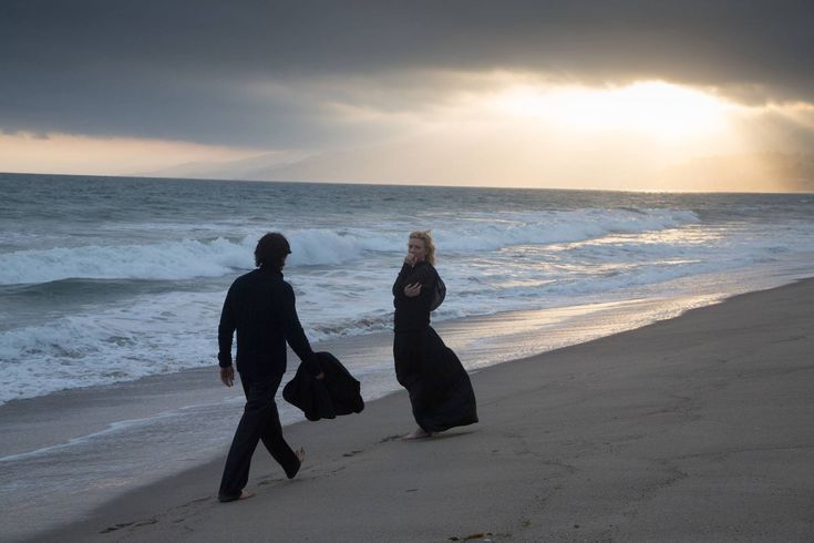 two people walking on the beach with their luggage