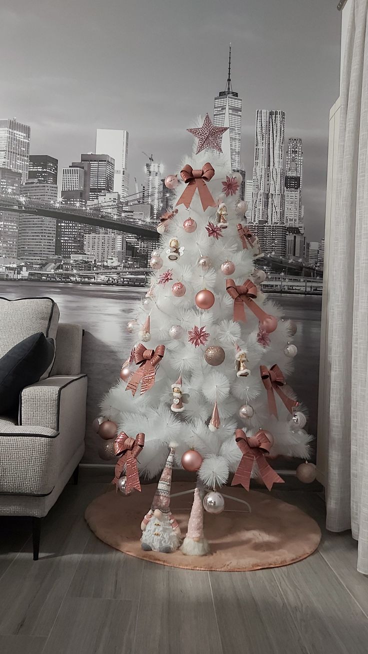 a white christmas tree with pink bows and ornaments in front of a cityscape