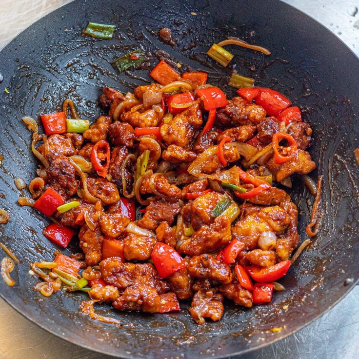 a wok filled with meat and vegetables on top of a table