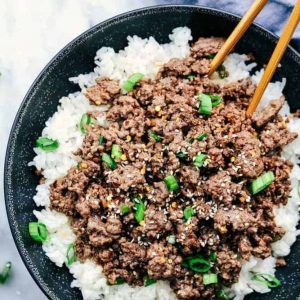 a black bowl filled with rice and ground beef next to chopsticks on the side