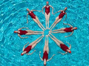 six people are floating in the blue water with their backs turned to the camera and arms extended