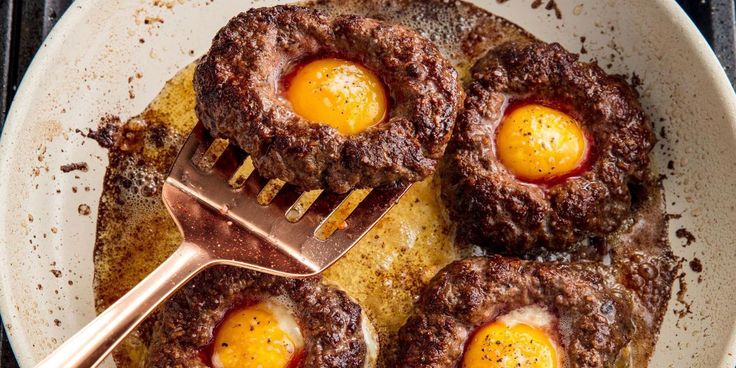 three eggs are in the middle of some meat patties on a skillet with a spatula