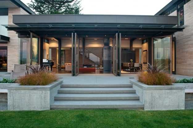 a modern house with steps leading up to the front door and patio area, surrounded by large concrete planters