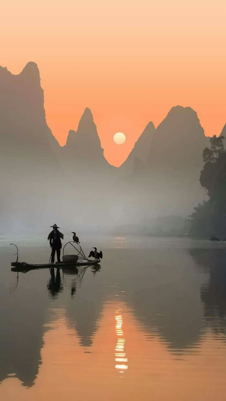 two people on a small boat in the water with mountains in the background at sunset