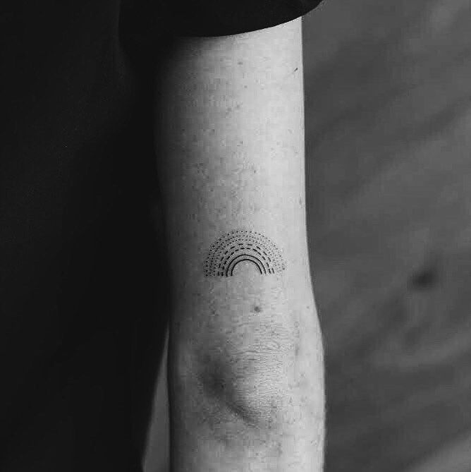 a black and white photo of a person's arm with a rainbow tattoo on it