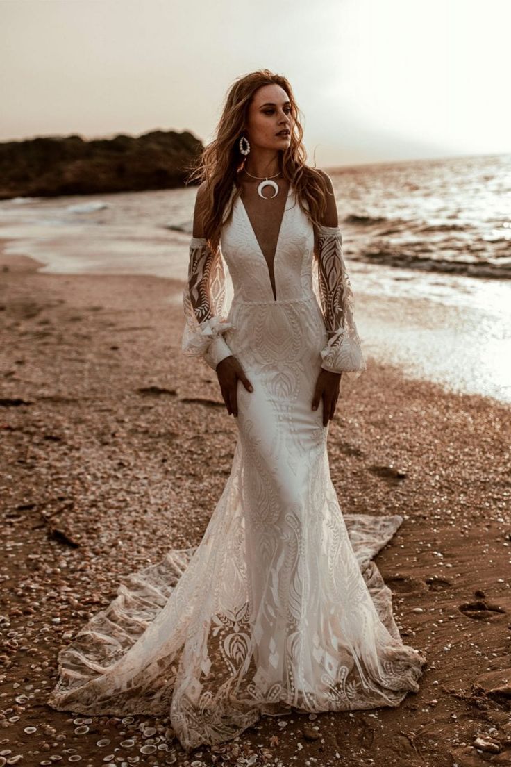 a woman standing on top of a beach next to the ocean wearing a white dress