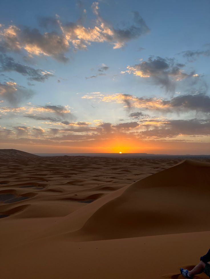 a person sitting on top of a sand dune in the desert at sunset or dawn